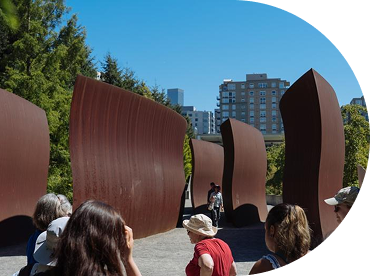 People explore an outdoor sculpture park with towering curved metal sculpture by Richard Serra under a clear blue sky.